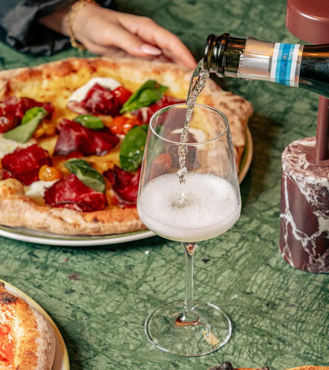 Prosecco versé dans un verre à côté d'une pizza napolitaine sur une table en marbre vert