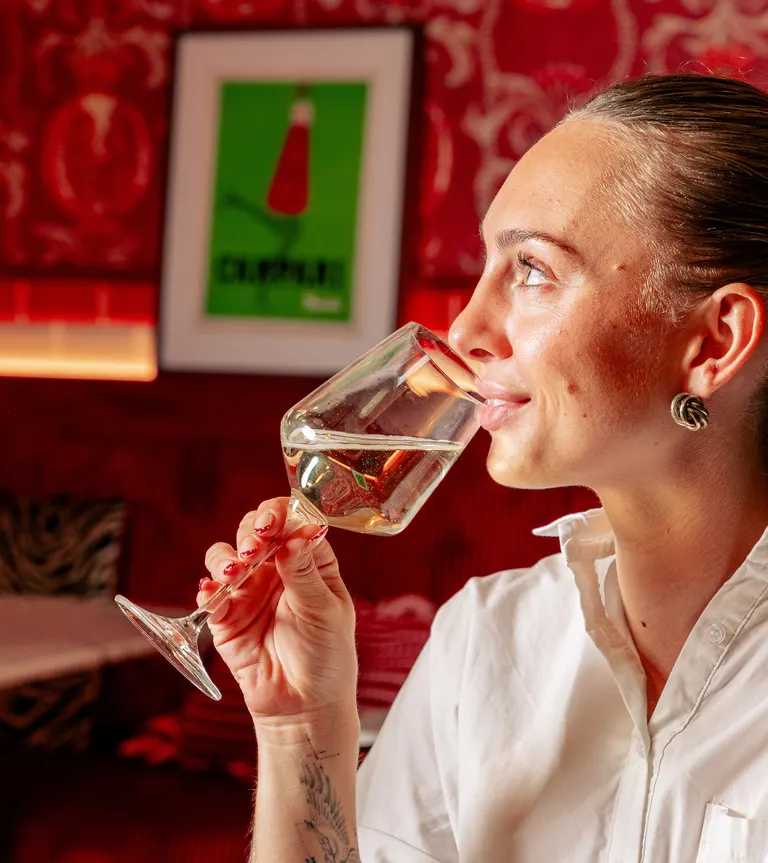 Une cliente goûte un verre de vin blanc devant l'affiche Campari