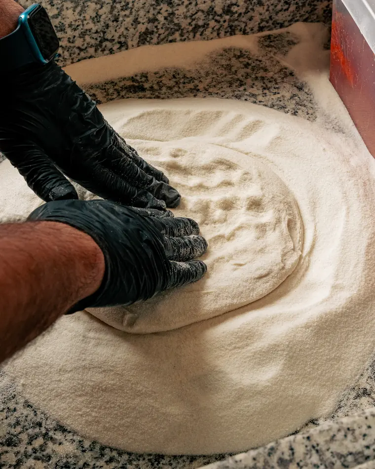 Mains gantées qui étalent la pâte à pizza dans la semoule