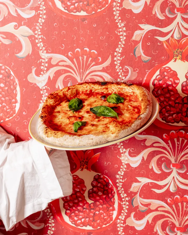 Pizza margherita au basilic servie devant le papier peint grenade de Scopertino