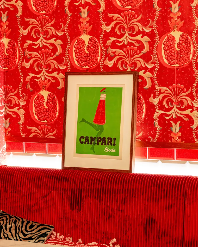 Banquette en velours rouge, affiche Campari et papier peint aux grenades