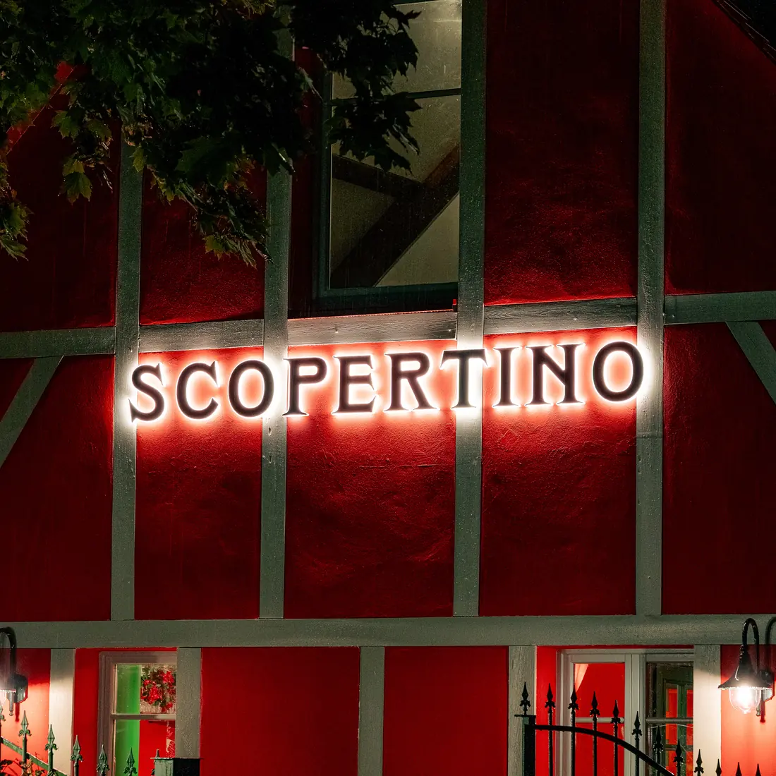 Façade rouge à colombages de Scopertino, enseigne lumineuse allumée le soir